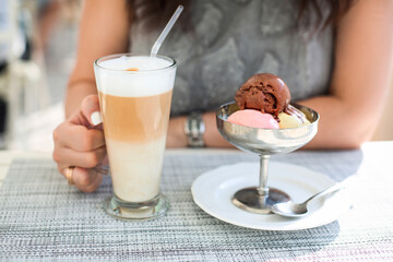 Woman drinking latte coffee and eating ice cream in outdoor cafe