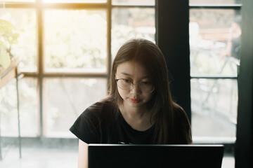 Young Asian girl wearing casual outfit is working on a laptop in an industrial room or cafe