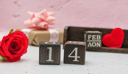 On a white and pink background, there are a rose, a heart, a gift and a calendar made of cubes with the date of February 14. Valentine's Day is celebrated in mid-February