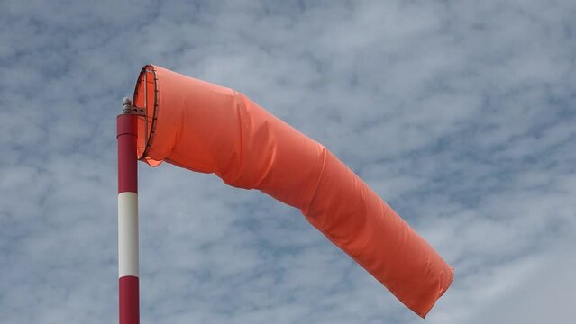 Windsock blow in wind to show speed and direction of wind gusts. Windsock with cloudy sky in the background. Conical tube in fabric used as a basic guide for the direction and speed of the wind.