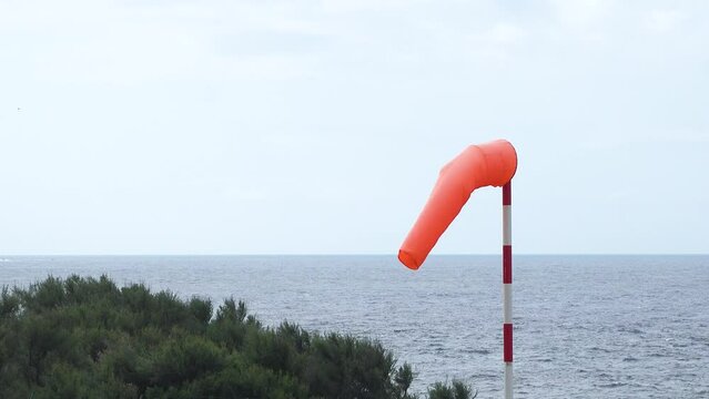 Windsock blow in wind to show speed and direction of wind gusts. Windsock with cloudy sky in the background. Conical tube in fabric used as a basic guide for the direction and speed of the wind.