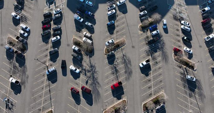 Overhead view of a parking lot with organized rows of cars casting long shadows.