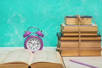 Alarm clock, open book and vintage books tied with twine. Education and wisdom concept