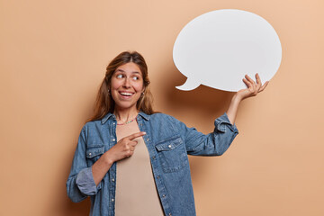 Horizontal shot of positive European woman with piercing in nose holds blank speech bubble shows...