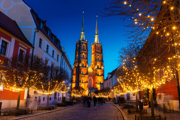 Street with cobblestone road, lights on trees, St. John the Baptist Cathedral with two spiers in...
