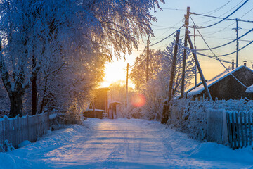 Winter frosty road in the village in the rays of the setting sun