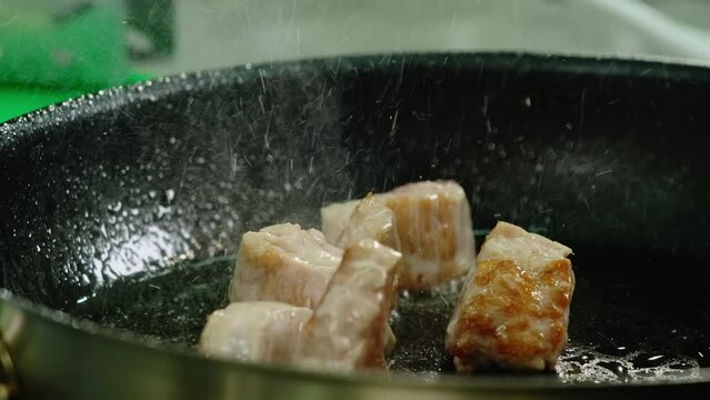 Splashing oil around searing juicy beef cubes with appetizing golden crust in teflon skillet. Professional cooking concept