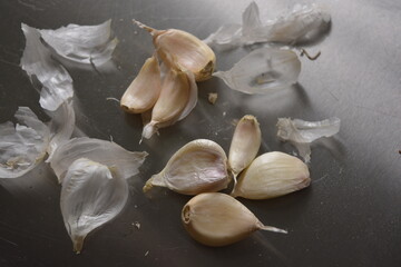 Dried white pieces, cloves of white garlic with dry peelings arranged on a metallic, reflective background.