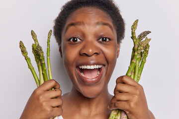 Young woman with short curly hair revels in joy of healthy eating holds asparagus stalks highlights...