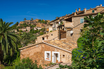 Fototapeta na wymiar Stunning cityscape of the small coastal village of Deia in Mallorca, Spain. Traditional houses terraced on hills surrounded by green trees. Tourist destinations in Spain. Balearic Islands.