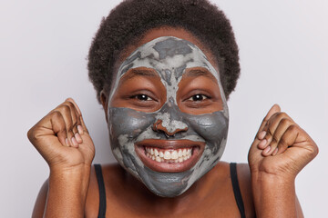 Close up shot of short haired woman with dark skin applies facial clay mask for skin rejuvenation...