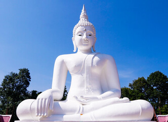 Big white buddha statue with trees on blue sky background in Thakhanun temple of  Kanchanaburi...