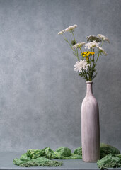 Still life with flowers. White wildflowers in a light tall vase on a light gray background....