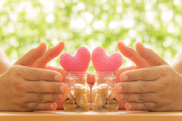 Man and woman hand hold gold coin in the two clear bottle with grow value as a pink hearts put on...