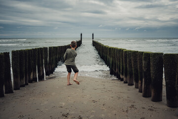 Junge wirft zwischen den Buhnen Steine in das Wasser - Strand von Domburg, Zeeland, Niederlande