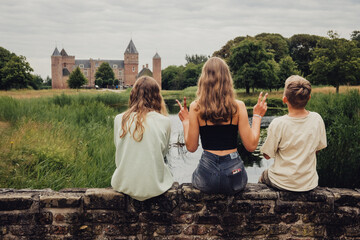 Drei Geschwister sitzen auf einer Mauer und schauen in Richtung Kasteel (Burg) Westhove, Domburg, Zeeland, Niederlande