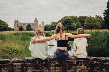 Drei Geschwister sitzen auf einer Mauer und schauen in Richtung Kasteel (Burg) Westhove, Domburg, Zeeland, Niederlande