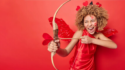 Horizontal shot of emotional female cupid takes aim with her bow and arrow gracefully shooting...