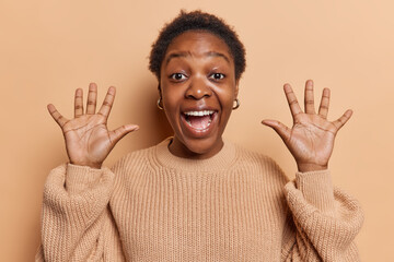 Happy dark skinned woman with short hair exclaims loudly keeps palms raised up reacts to awesome...