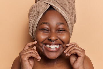 Indoor close up of happy smiling broadly African american girl after shower with towel on head...