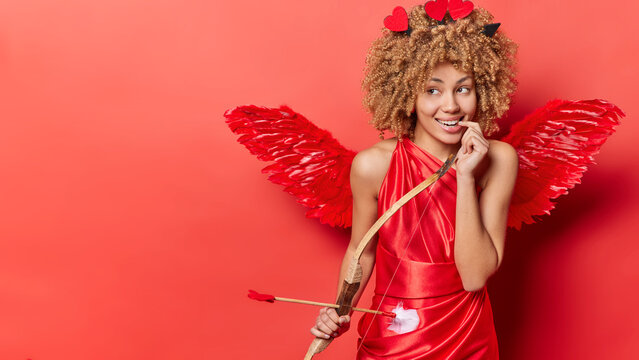 Happy St. Valentines Day. Studio shot of young pretty cheerful smiling African american girl standing on right in cupid costume looking at blank space for promotion thinking about something pleasant