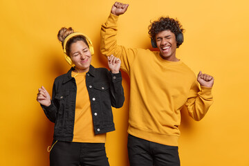 People and entertainment. Indoor photo of young happy excited smiling Hindu man and European woman listening to music on headphones dancing wearing casual black and yellow clothes with closed eyes
