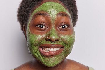 Indoor shot of happy smiling young African american girl doing beauty procedure applying face...