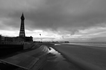 A moody Black and white photo along Blackpool beach with the pier and tower in silhouette - 701418382