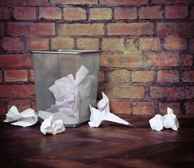 Recycle bin filled with crumpled papers. Brick wall background