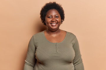 Portrait of cheerful plump adult African woman with short dark curly hair smiles pleasantly being...