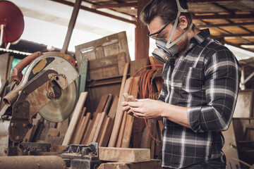 Male carpenter wearing protective mask using electric circular saw cutting wood board at the...