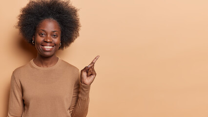 Horizontal shot of pretty dark skinned young woman points finger on left shows blank space for your...