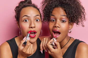 Women beauty and cosmetology concept. Photo of wondered young women put on lipstick uses...