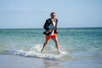 business success of businessman. Businessman in suit with laptop running in sea. successful businessman in wet suit at beach. businessman running at summer vacation. business traveler