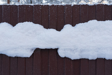 Fragment of a brown metal fence. In the middle there is a wide white stripe of adhered snow with jagged edges. Background. Form.