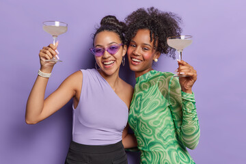 Joyful young women exude carefree vibes as they dance embrace and raise cocktail glasses in...