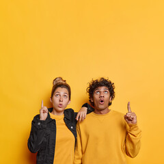Vertical shot of impressed young woman and man indicate above on copy space show something stunning keep mouth opened from amazement isolated over yellow studio background. Wow its unbelievable © WHstudio Leushin N
