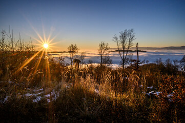 Sunset over the winter landscape. Inverse weather with fog in the valleys. The sun with sun rays in...