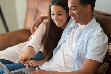 Young couple moving to a new home relaxing sitting on the sofa using computer laptop, smiling happy...