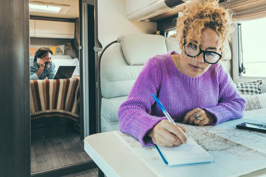 woman writes and plans sitting inside the camper while husband relaxes watching a film