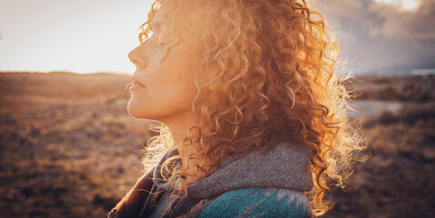 Side portrait of beautiful middle age blonde woman with long curly hair and closed eyes enjoying sunset in outdoors travel leisure activity alone. Wanderlust and interior balance happiness and freedom - obrazy, fototapety, plakaty