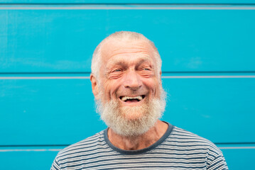 75 year old senior man laughs while having a good time outdoors. Portrait with blue background....
