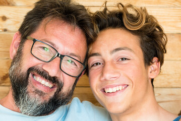 Head shot happy teenager son embracing shoulders of happy middle aged father, looking at camera....