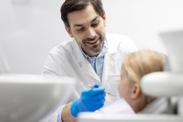 Cheerful male dentist checking the teeth of girl teenager, preparing for dental treatment in clinic