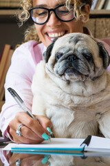 Happy woman at home in love for her best friend pug dog while work at the computer laptop on the...
