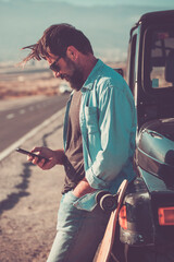 Young handsome man use phone cellular outside the black car vehicle with long road in background -...