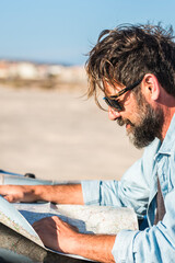 Man look a paper road trip map standing outside the car with blue sky and ground desert in...