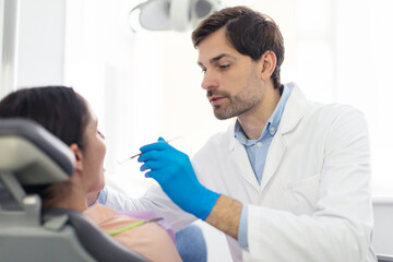 Professional male dentist doctor making regular check up for female patient in modern dental clinic
