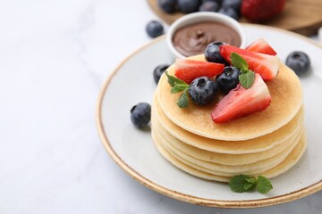 Delicious pancakes with strawberries, blueberries and chocolate sauce on light table, closeup. Space for text