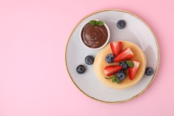 Delicious pancakes with strawberries, blueberries, mint and chocolate sauce on pink background, top view. Space for text